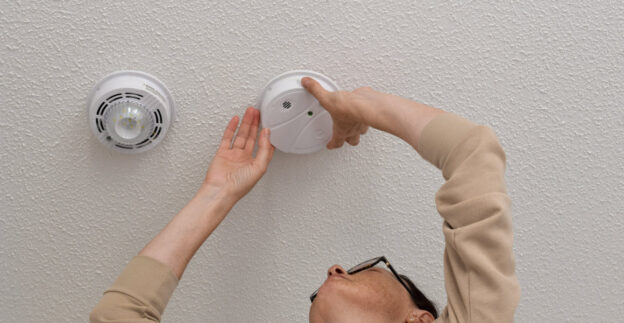 Person changing smoke alarm on ceiling