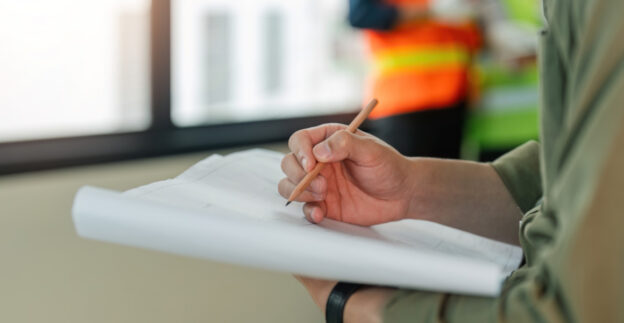 Man writing on building plans with strata building in background