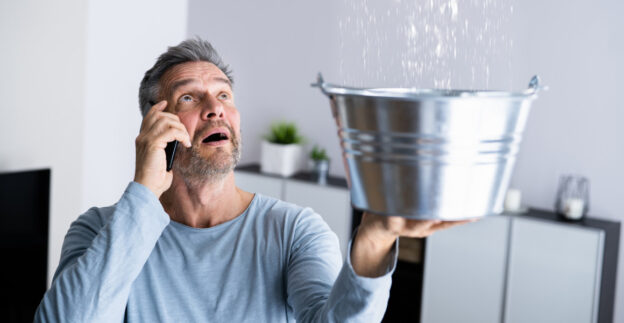 Man catching leak from ceiling in bucket whilst making phonecall